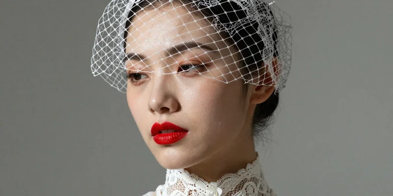 Close up portrait of a stylish modern bride wearing a short, chic upcycled birdcage veil made from vintage lace, bold red