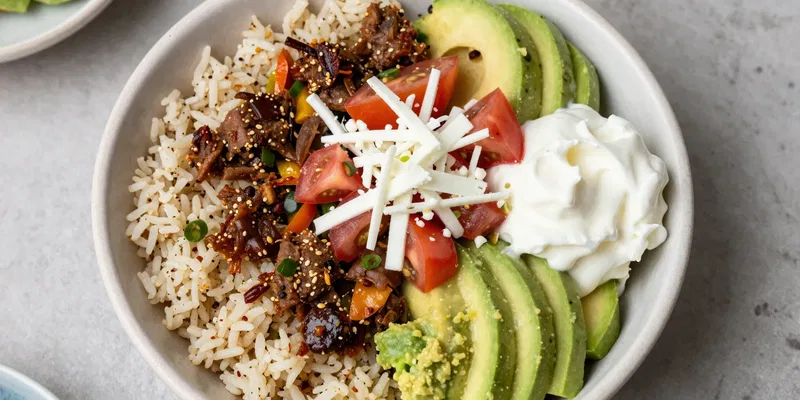 Beautifully composed keto Chipotle bowl: cilantro-lime cauliflower rice topped with carnitas, fajita veggies, fresh tomato