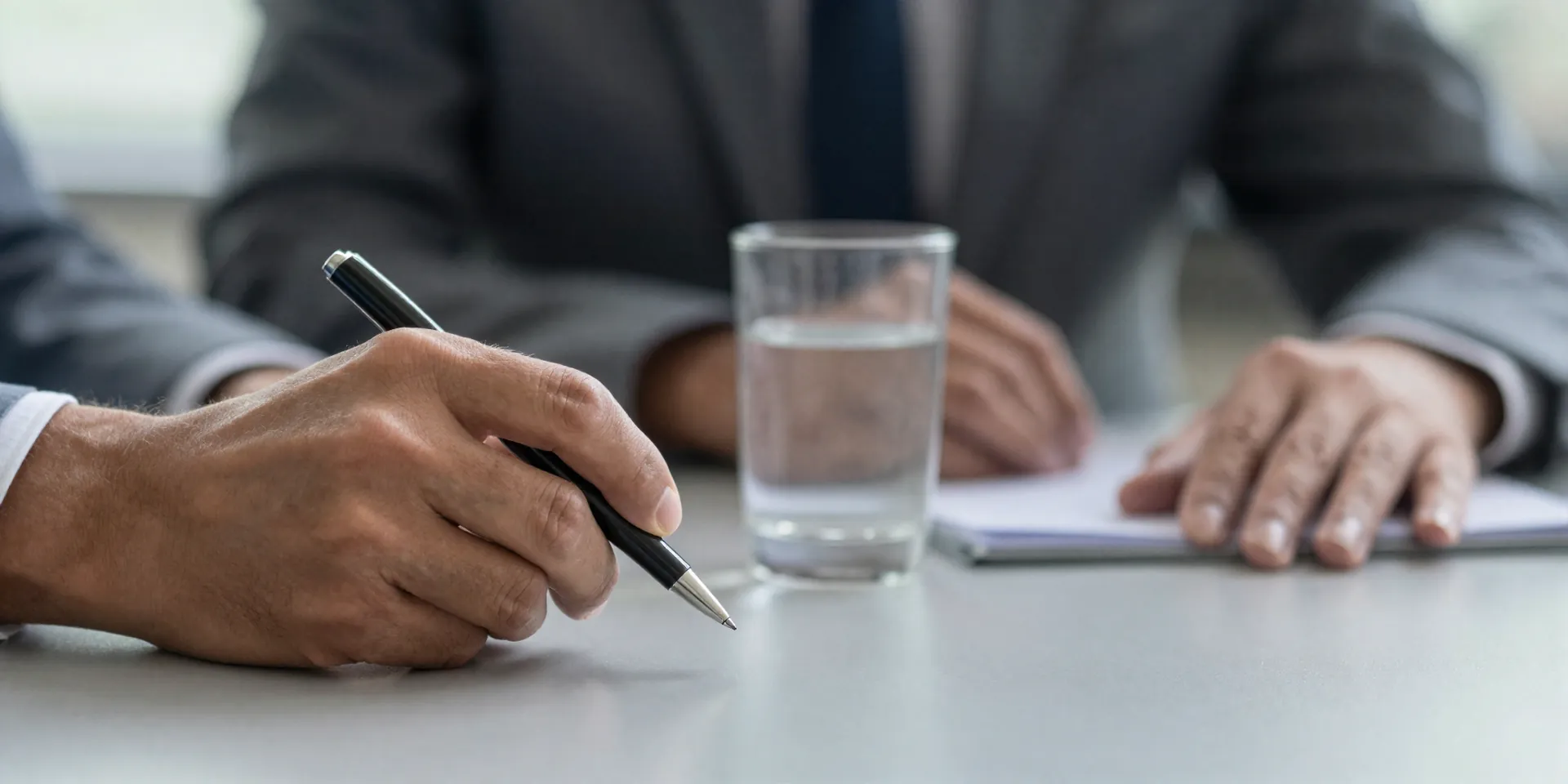 Close-up of a calm, focused executive's hands on a conference table during a tense meeting. One hand is loosely gripping