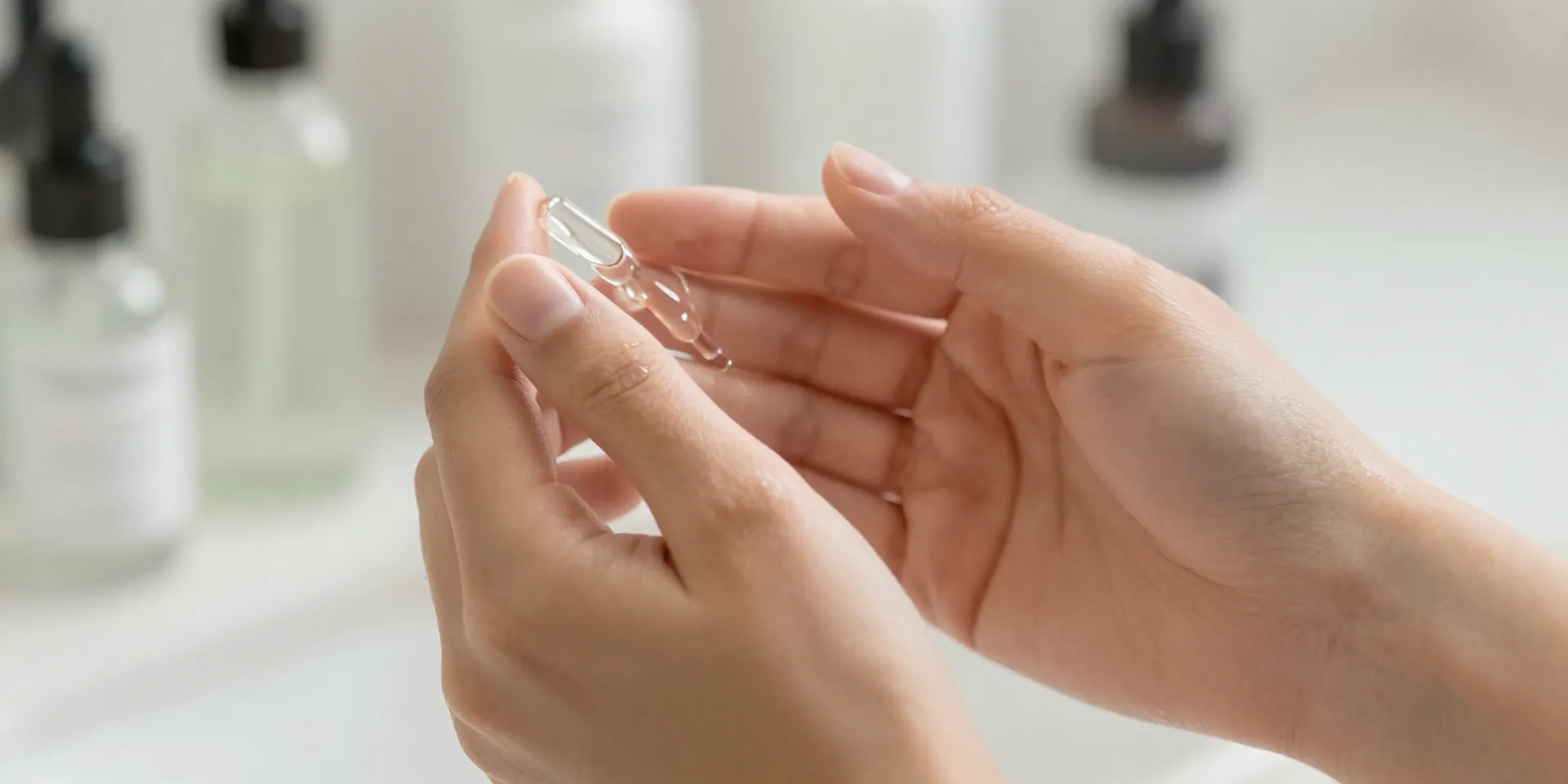 Close-up macro shot of woman's hands applying a dewy translucent serum to her cheek, glowing healthy skin, bathroom setting