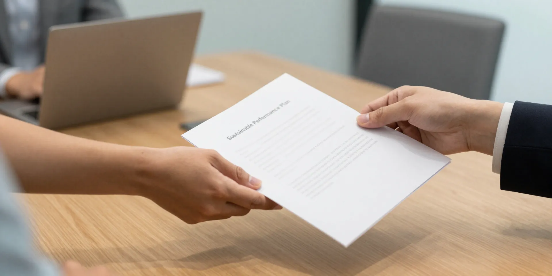 A modern, office meeting room. Two hands, one of an employee and one of an HR representative, are shaking over a simple