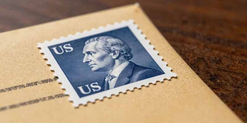 US postage stamp being placed on a textured envelope. indoor lighting, high detail